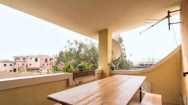 Un balcón con mesa y bancos de madera, una antena parabólica y vistas a edificios y zonas verdes.