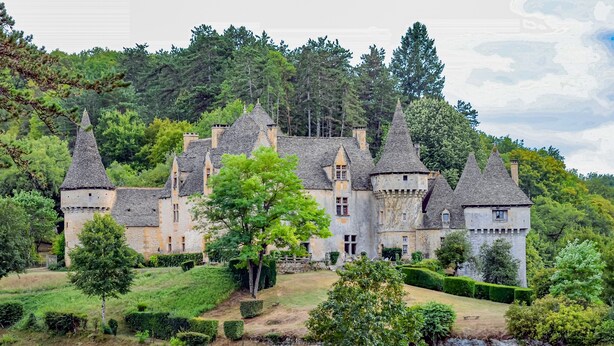 Un castillo con múltiples torres, rodeado de exuberante vegetación y un jardín cuidado.