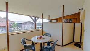 Una habitación con una mesa redonda y cuatro sillas, una ventana que da a vistas de edificios, y paneles de madera en las paredes.
