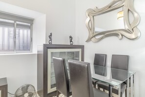 A dining area with a glass table and chairs, a decorative mirror, and a window with blinds.