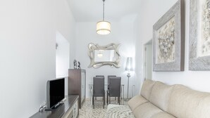 Un salon avec un canapé, un téléviseur posé sur un meuble, une table à manger avec des chaises et un miroir accroché au mur.