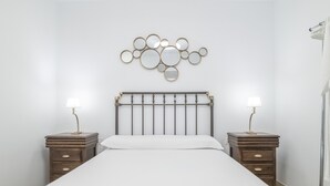 Une chambre à coucher comprenant un lit, deux tables de chevet, un miroir fixé au mur et un porte-serviettes suspendu.