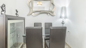 Un coin repas comprenant une table en verre, quatre chaises, un miroir décoratif et une lampe fixée au mur.