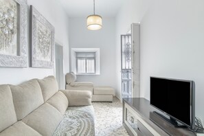 A modern living room with a sofa, a flat-screen TV, a patterned rug, and wall art.