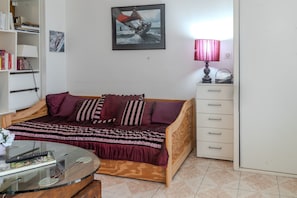 Un dormitorio con cama, mesita de noche, lámpara, estantería y un cuadro en la pared.