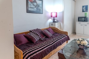 Un dormitorio con una cama de madera, una mesita de centro de vidrio con un jarrón, una lámpara y un televisor sobre un mueble.