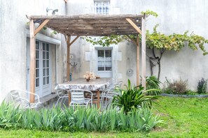 A covered patio with a table and chairs, a pergola, and a garden with plants and a wall. - Holiday Home 'La Maison De Joséphine' with Private Terrace and Wi-Fi (Montignac-Charente)