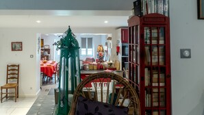 A room with a wicker chair, a red telephone booth, and a dining area in the background.
