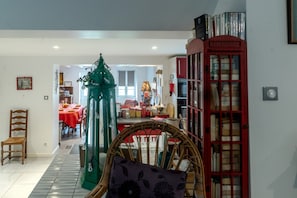 A room with a wicker chair, a red telephone booth, and a dining area in the background.
