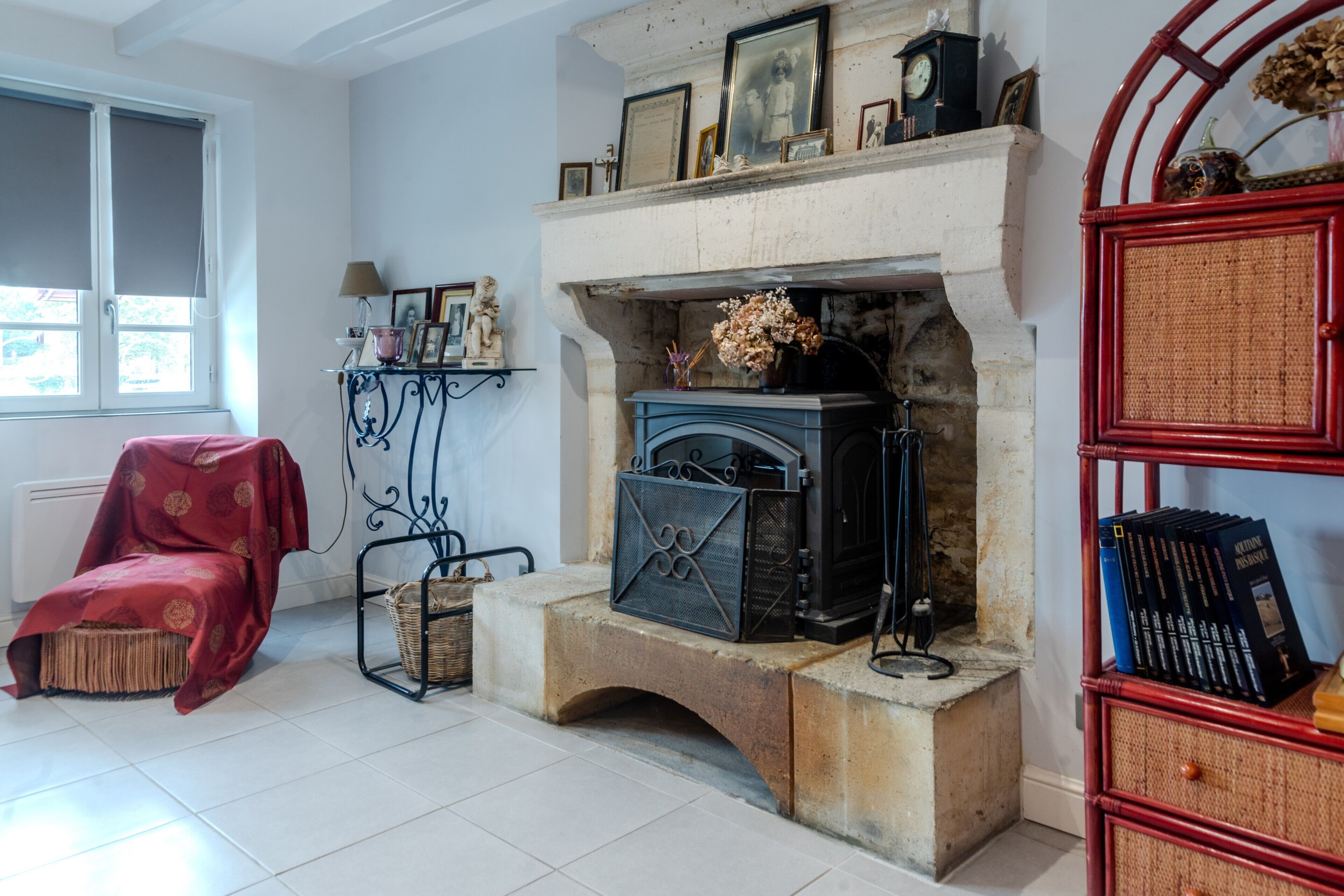 A room with a fireplace, a red armchair, a bookshelf, and a window.