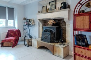 Um quarto com lareira, uma poltrona vermelha, uma estante de livros e uma janela.