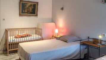 A bedroom with a crib, a bed, a nightstand with a lamp, and a wall-mounted picture.