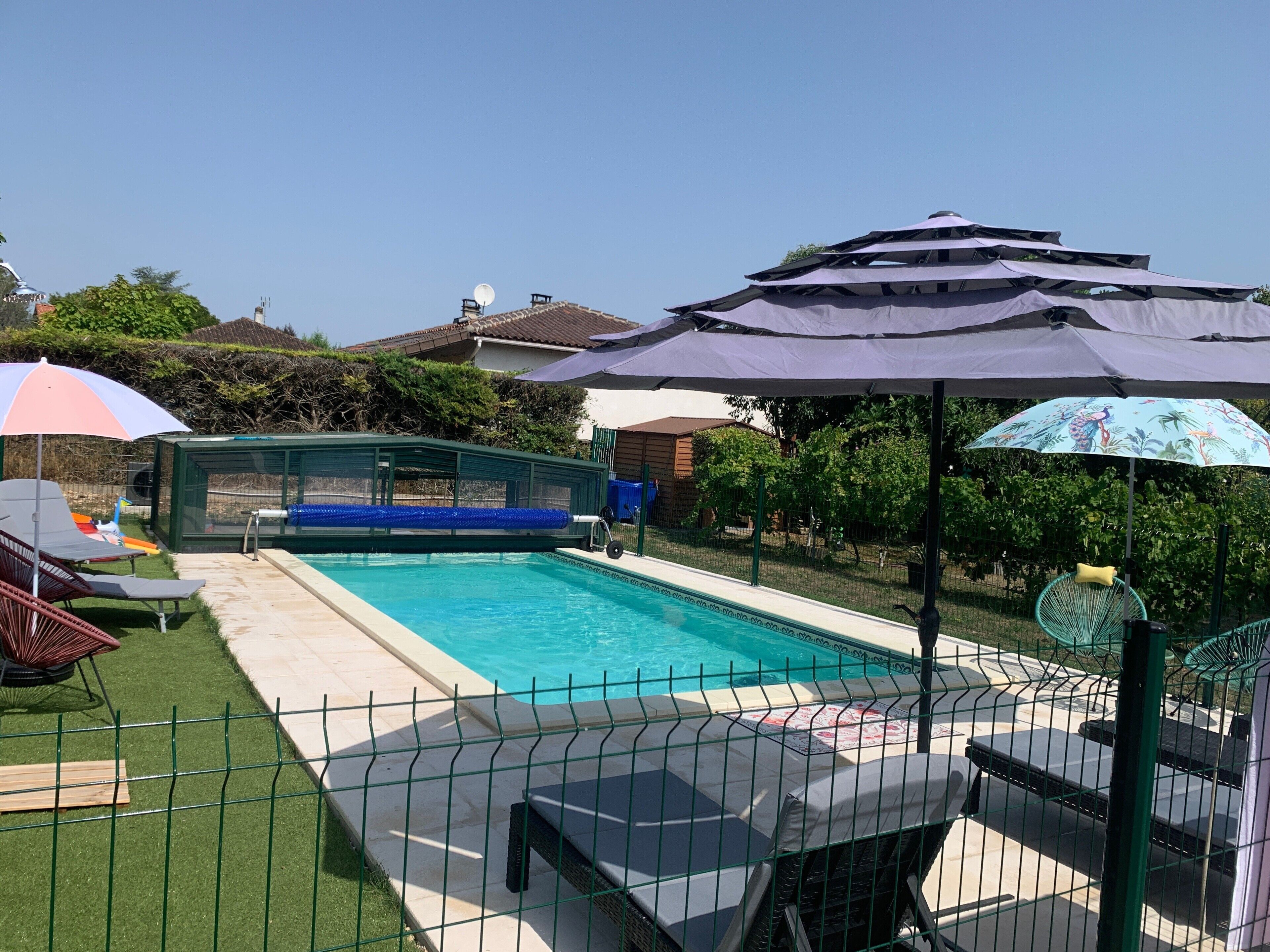 A swimming pool with a green fence, lounge chairs, and umbrellas.