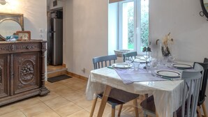 A dining area with a table set for four, a wooden cabinet, and a window with a view of greenery. - Holiday Home 'La Maison D'Éloi' with Shared Pool, Private Terrace & Wi-Fi (Montignac-Charente)