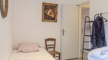 Una habitación con una cama, una silla, una puerta, un perchero y un cuadro en la pared.