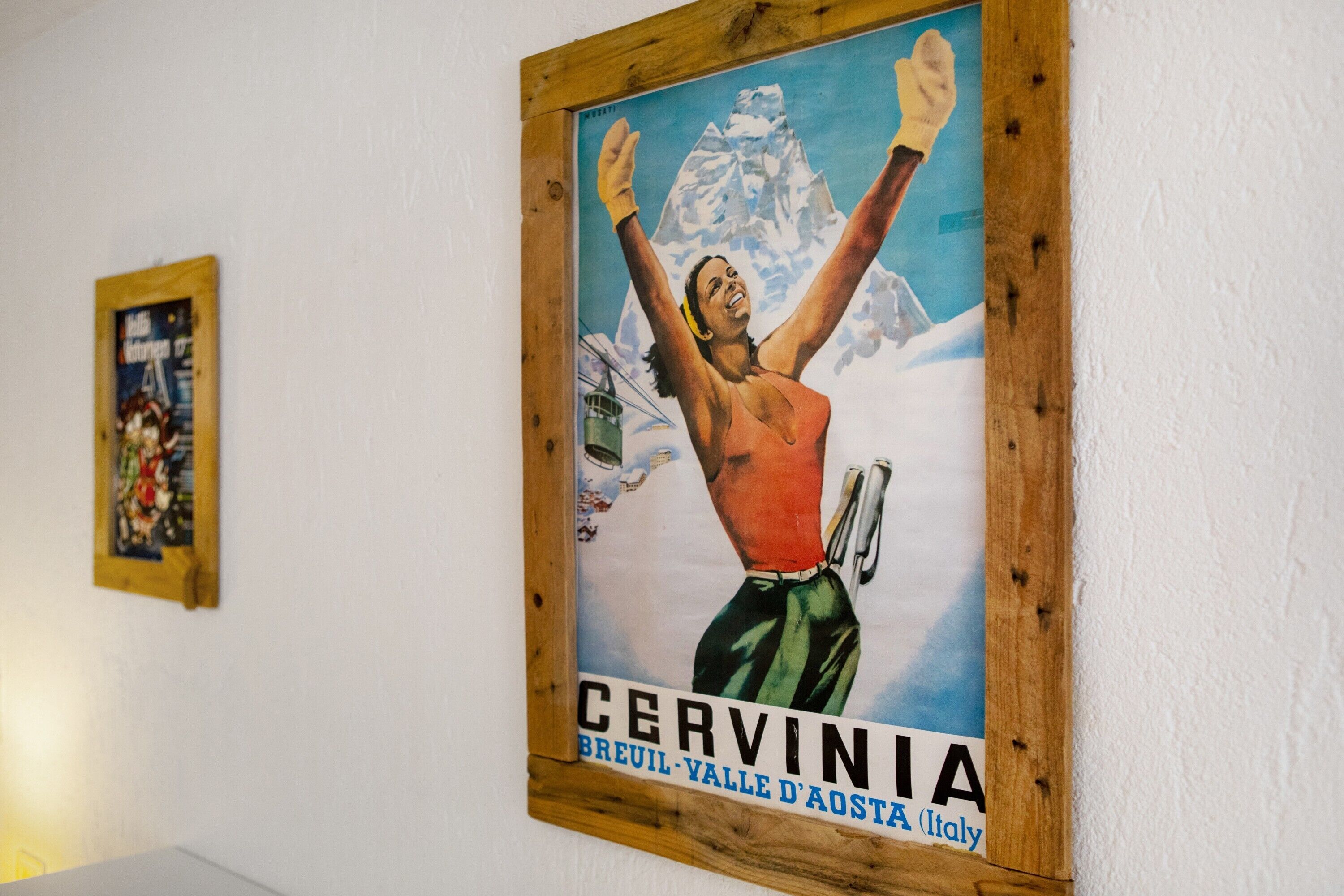 En inramad affisch med ett berg och en person som har armarna lyfta, med texten ”CERVINIA” och ”BREUIL – VALLE D’AOSTA (Italien)”.