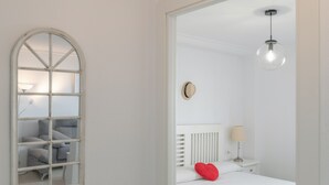 A white room with a bed, a bedside lamp, a round mirror, and a hanging light fixture. - Casa Ricardo - Vacation Home Near the Beach in Barbate (Barbate)