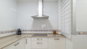 A kitchen with white tiles, a stainless steel range hood, a coffee maker, and a decorative tile border. - Casa Ricardo - Vacation Home Near the Beach in Barbate (Barbate)