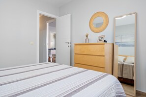 Une chambre à coucher comprenant un lit, une commode, un miroir et une porte donnant sur une autre pièce.
