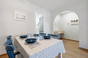Un coin repas avec une table dressée pour quatre personnes, des chaises, un tableau encadré au mur et un miroir au-dessus de l’évier.