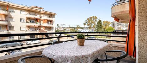 Ein Balkon mit Tisch und Stühlen, einem Blumentopf und Blick auf die Straße und Häuser.