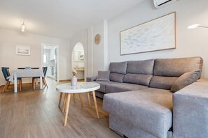 Un salon avec un canapé gris, une table basse ronde, une table à manger avec des chaises et un tableau accroché au mur.