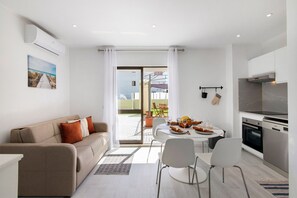 A modern living room with a sofa, dining table, chairs, and a kitchen area with appliances.
