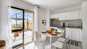 A modern kitchen with white cabinets, a dining area with a table and chairs, and a view through a glass door to an outdoor patio. - Apartment 'Penthouse Paradise - Praia Da Rocha' with Sea View, Wi-Fi and Air Conditioning (Portimão)