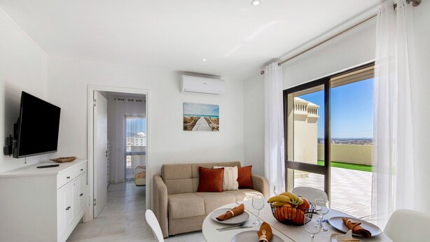 A modern hotel room with a dining area, a sofa, a flat-screen TV, and a large window with a view. - Apartment 'Penthouse Paradise - Praia Da Rocha' with Sea View, Wi-Fi and Air Conditioning (Portimão)