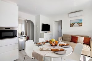 A modern kitchen with white cabinets, a built-in oven, and a flat-screen TV.