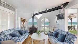 Une pièce avec deux canapés à rayures, une table blanche, une cheminée et de grandes fenêtres donnant sur la mer.
