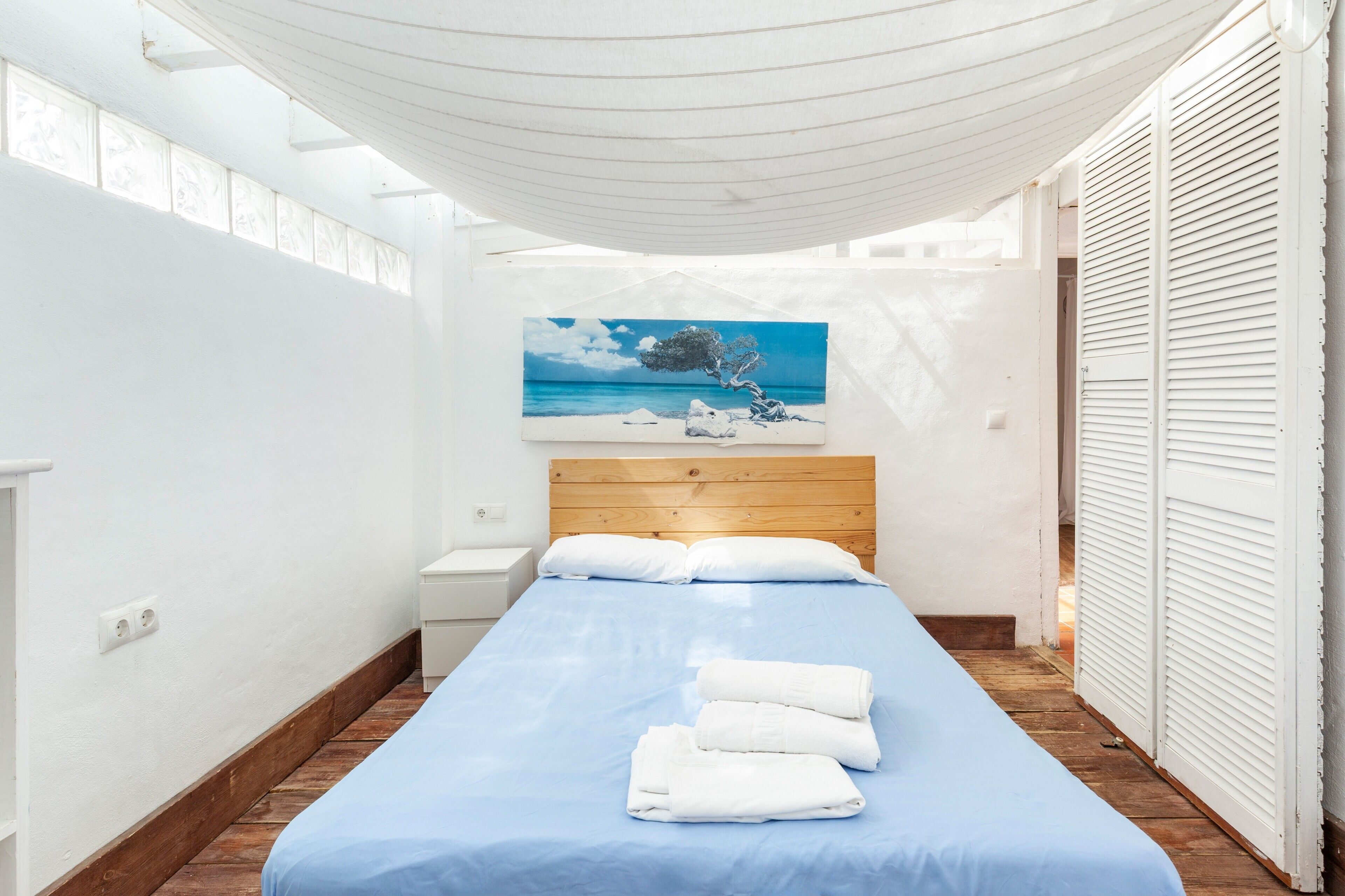 A narrow room with a bed, a painting, and a white canopy.