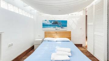 A narrow room with a bed, a painting, and a white canopy.