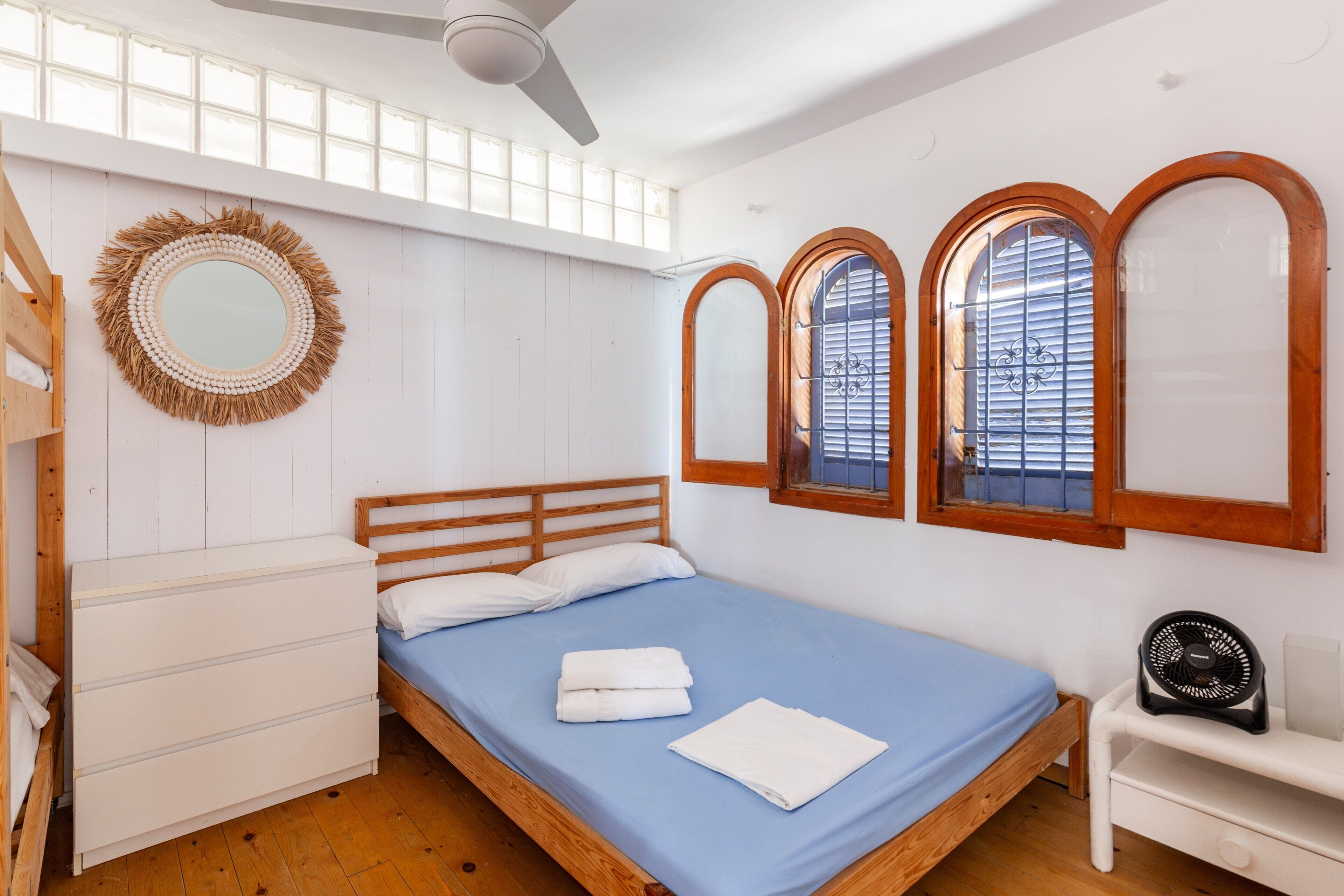 A bedroom with a bed, a dresser, a mirror, and a window with wooden frames.