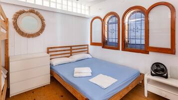 A bedroom with a bed, a dresser, a mirror, and a window with wooden frames.