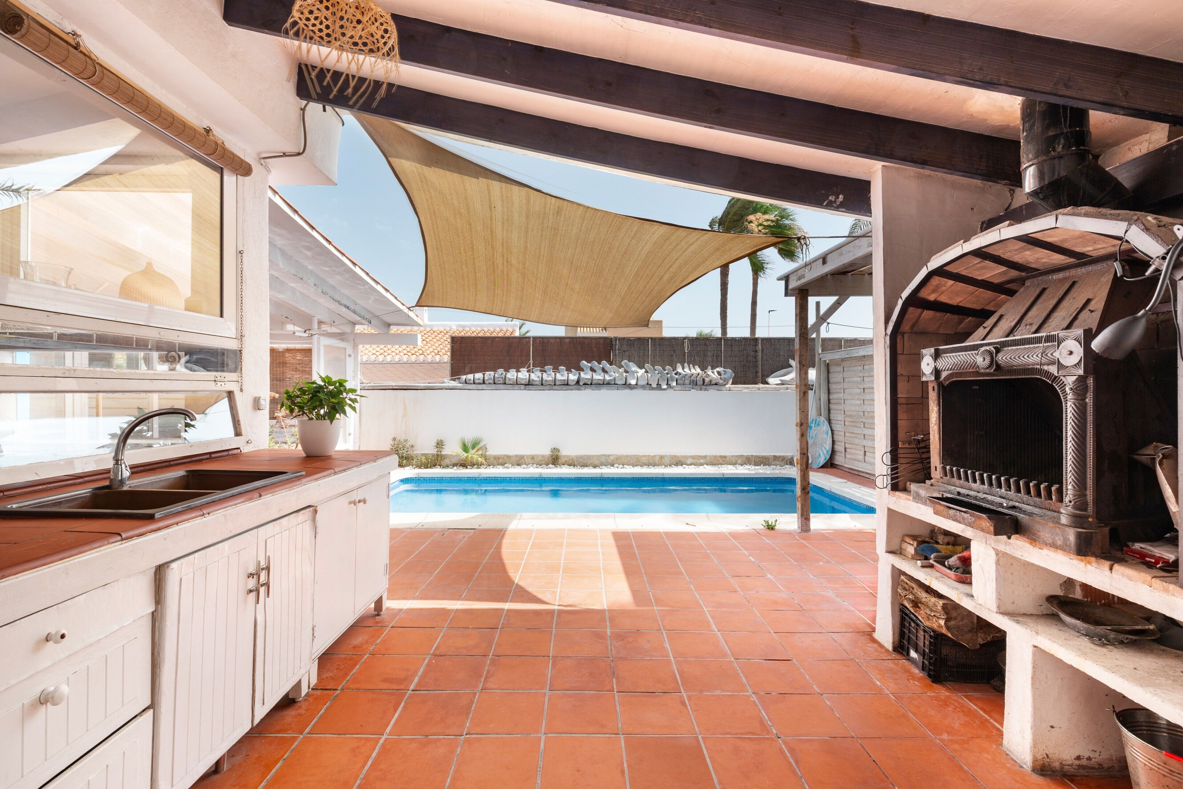 A kitchen with a sink, a barbecue grill, and a pool in the background.