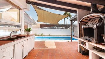 A kitchen with a sink, a barbecue grill, and a pool in the background.