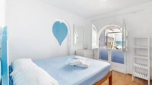 Une chambre à coucher avec un lit, une décoration en forme de cœur, une armoire blanche et une vue sur l’extérieur par une porte ouverte.