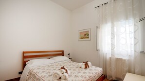 Un dormitorio con una cama de madera, una mesita de noche, una lámpara pequeña y una ventana con cortina.