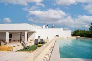 A poolside area with a white building, outdoor seating, and a clear sky.