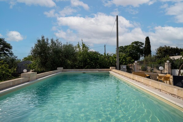 A rectangular swimming pool with clear water, surrounded by a concrete deck and a fence.