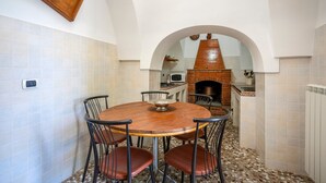 Un coin repas comprenant une table ronde en bois, quatre chaises, un petit four en briques et un mur recouvert de carreaux.