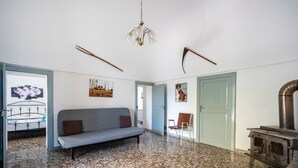Une pièce avec un canapé gris, une chaise en bois, un mur décoratif, une porte et un poêle d’époque.
