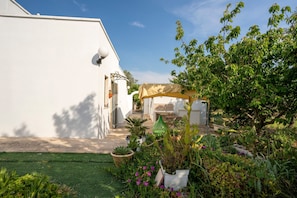 Un bâtiment blanc doté d’un espace extérieur aménagé avec des tables et des chaises, de plantes en pot et un ciel dégagé.