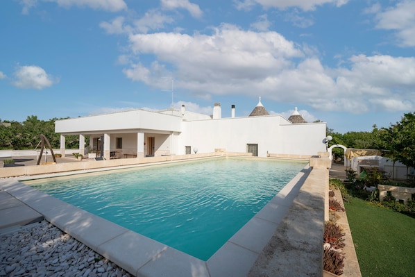 Un bâtiment moderne doté d’une piscine, d’un patio couvert et d’une pelouse bien entretenue.