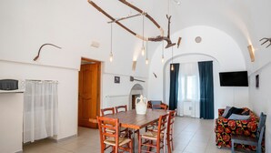 A dining area with a wooden table and chairs, a white pitcher, and a TV mounted on the wall.