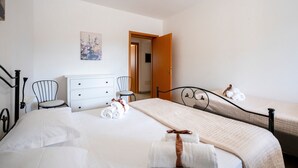 A hotel room with a bed, two bedside tables, a dresser, a chair, and a door leading to another room.