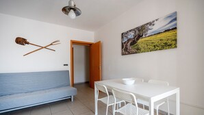 Una stanza con un divano blu, un tavolo da pranzo bianco con sedie, un quadro raffigurante un paesaggio e un lampadario.