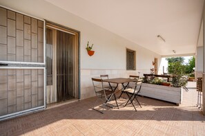 A patio with a table and chairs, a bench, potted plants, and a sliding door.