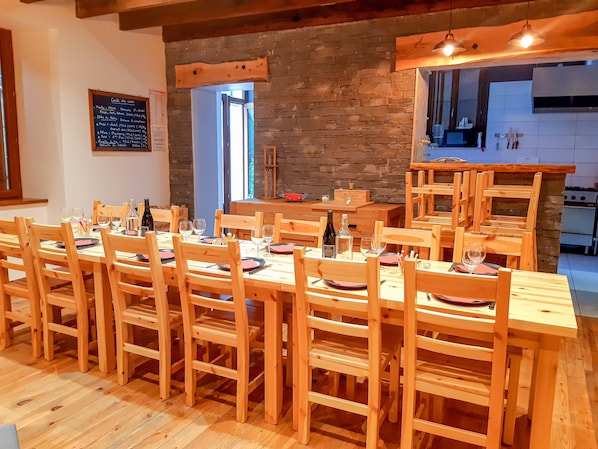 Un restaurant avec des tables et des chaises en bois, un mur en pierre et une cuisine visible à travers une porte ouverte.